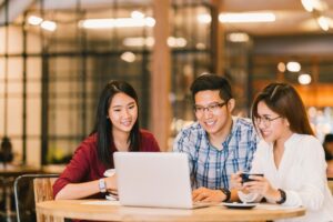 Three people sitting at a table looking at a laptop.